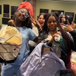 two participants holding new back-to-school backpacks with mentor